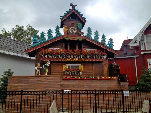 A whimsical wooden building with a clock, surrounded by trees and flowers, resembling a fairytale cottage.