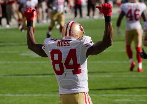 A football player in a red and white jersey raises his arms in celebration on the field.