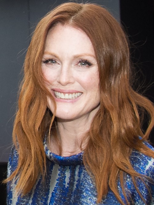 A smiling woman with long, wavy red hair wearing a blue patterned dress.