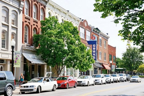 A charming street lined with historic brick buildings, trees, and parked cars, featuring a sign for "Gray's."