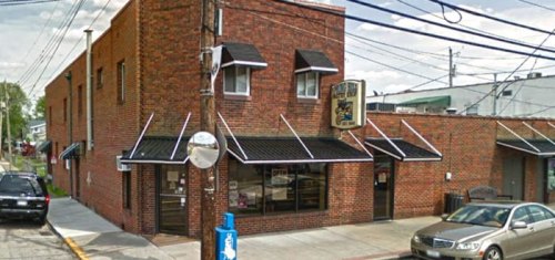 A brick building with awnings, featuring a sign, located on a street with parked cars and utility poles.