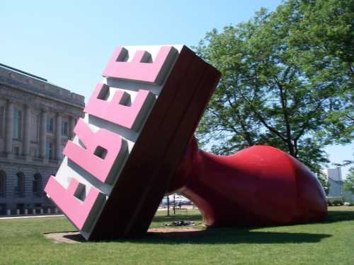 A large, tilted red rubber stamp with the word "FREE" in pink letters, set on green grass near a building.