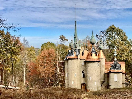 A whimsical castle with spires and a copper roof, surrounded by colorful autumn trees under a blue sky.