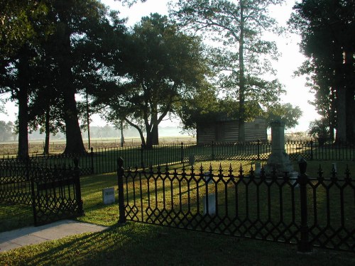 A serene cemetery with a wrought iron fence, surrounded by trees and a misty landscape in the background.