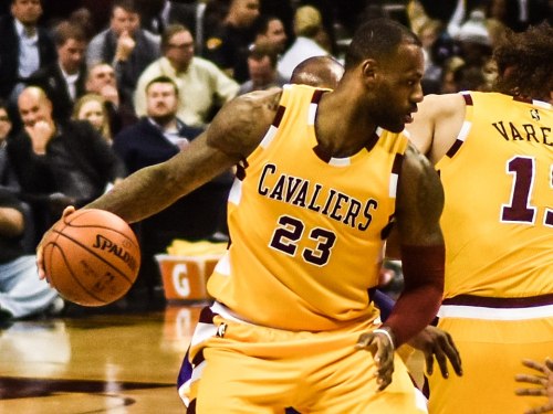A basketball player in a yellow Cavaliers jersey dribbles the ball during a game.