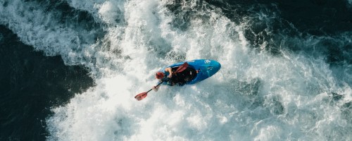 Aerial view of a kayaker navigating through white water waves.