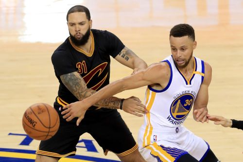 Two basketball players compete for the ball during a game, one in a black jersey and the other in a yellow and blue jersey.