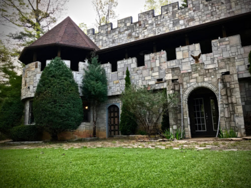A stone castle with a turret, surrounded by greenery and a well-maintained lawn.