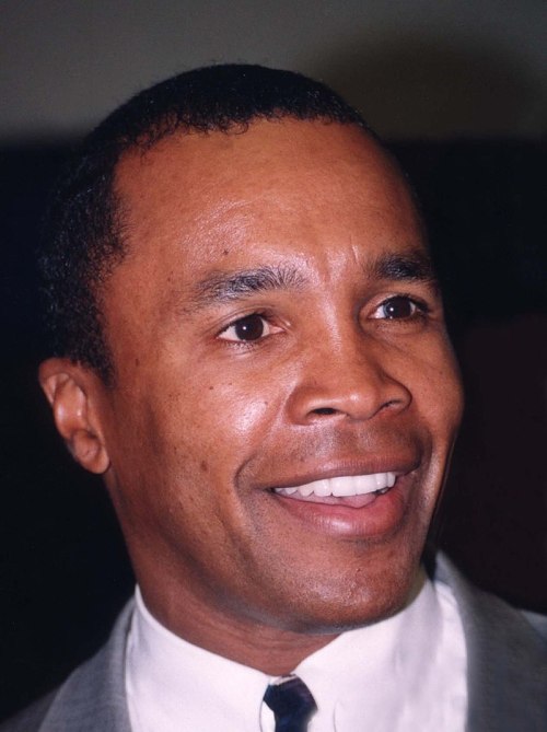 A smiling man with short hair, wearing a suit and tie, appears cheerful in a close-up portrait.