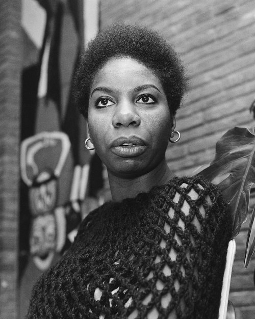 A black and white portrait of a woman with short hair, wearing a textured top, gazing thoughtfully at the camera.