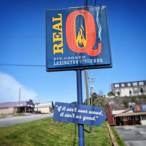 Sign for "Real Q" BBQ featuring a flame logo and the slogan: "if it ain't over wood, it ain't as good."