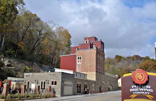 Potosi Brewing Company building with a red roof, surrounded by trees and a cloudy sky. Sign in foreground.