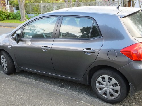 A gray hatchback car parked on the street, showing its side profile and wheels.