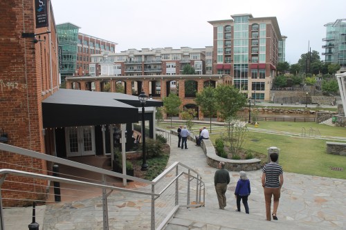 A scenic view of a brick building with a modern backdrop, featuring a pathway and people walking in a green area.