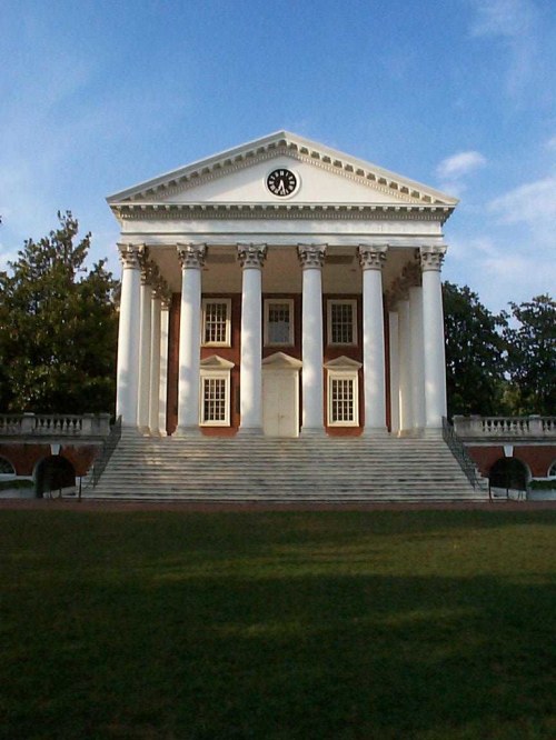 A grand building with a clock, featuring tall white columns and a staircase, set against a blue sky.