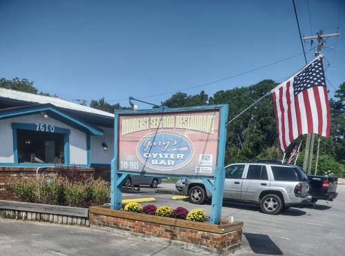 Sign for Gary's Oyster Bar outside a seafood restaurant, with an American flag and colorful flowers in the foreground.