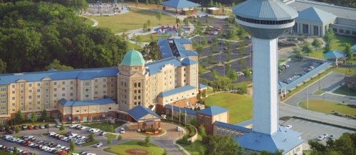 Aerial view of a hotel with a water tower, surrounded by green spaces and a playground in the background.