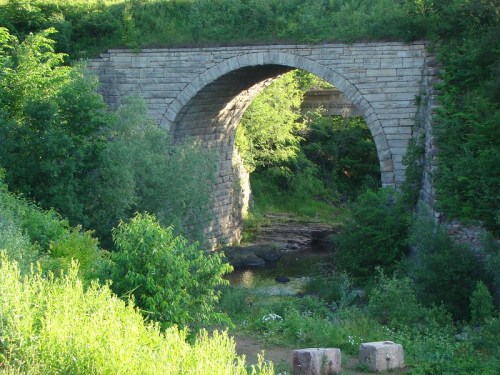 Stone arch bridge surrounded by lush greenery and a calm stream below.