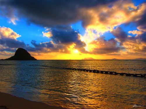 A vibrant sunset over the ocean, with clouds reflecting colors and a silhouette of a distant island.
