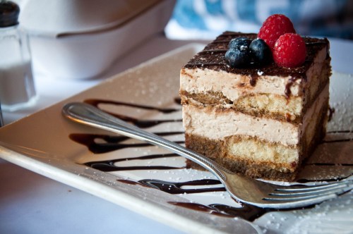 A slice of layered dessert topped with raspberries and blueberries, drizzled with chocolate sauce on a white plate.
