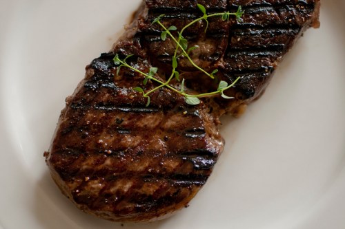 Grilled steak on a white plate, garnished with fresh thyme sprigs.