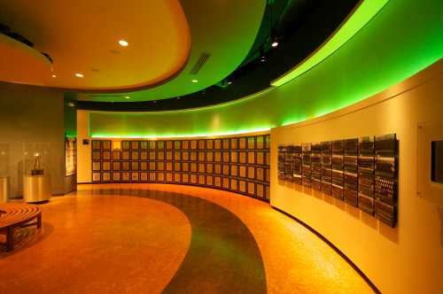 A curved wall displays plaques and panels under green lighting in a modern, spacious interior.