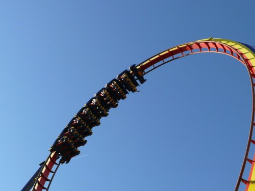 A roller coaster reaches the top of a loop against a clear blue sky, with riders enjoying the thrill.
