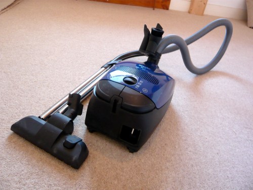 A blue vacuum cleaner with a hose and nozzle resting on a beige carpet.