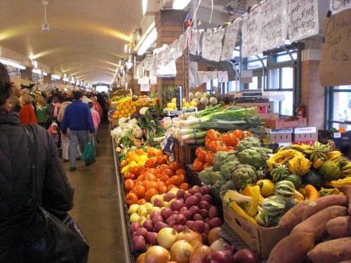A bustling market aisle filled with colorful fruits and vegetables, with shoppers browsing the stalls.