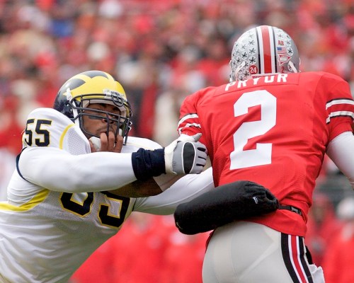 A football player in a blue jersey tackles a player in a red jersey during a game.