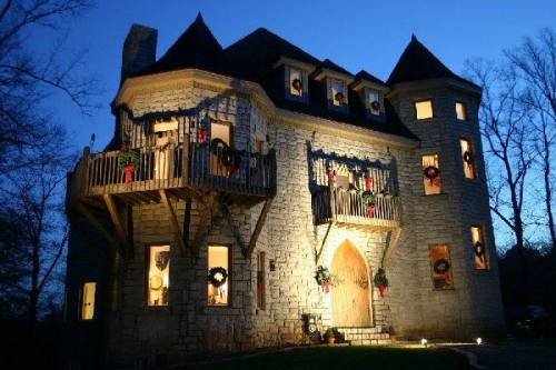 A stone castle with balconies, decorated for the holidays, illuminated at dusk with wreaths on the windows.