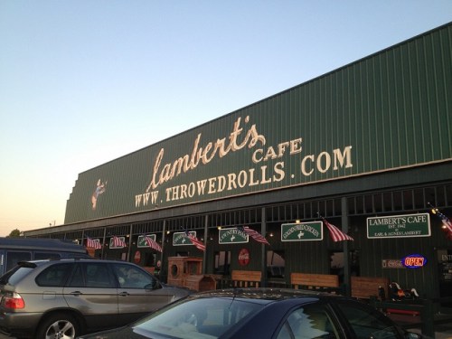 Exterior of Lambert's Cafe with a green facade, signs, and flags, under a clear sky at sunset.