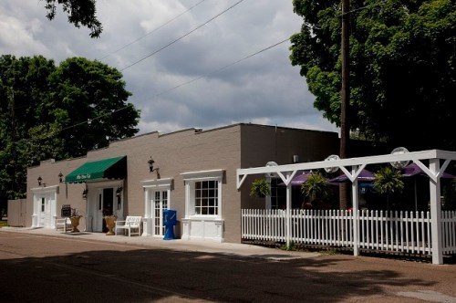 A quaint building with a green awning, white trim, and a picket fence, set against a cloudy sky.