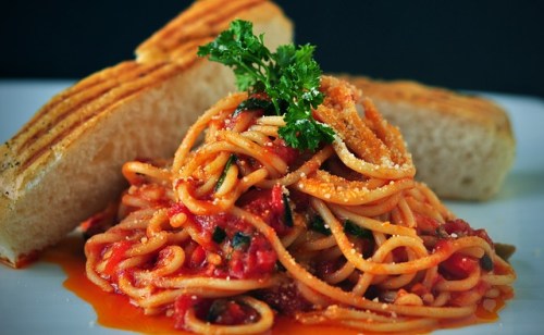 A plate of spaghetti with marinara sauce, garnished with parsley, served with two slices of toasted bread.