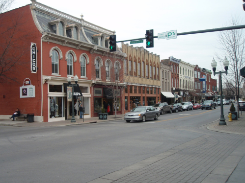 A street view of a historic downtown area with shops, cars, and traffic lights on a cloudy day.