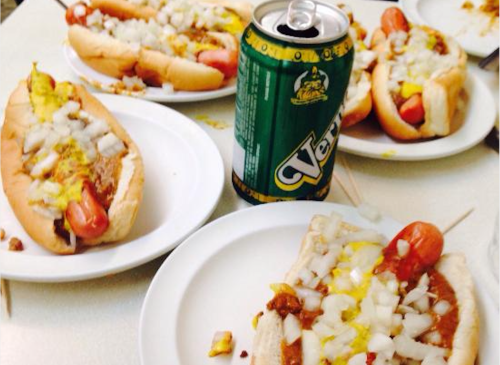 A table with several hot dogs topped with onions and mustard, alongside a can of soda.