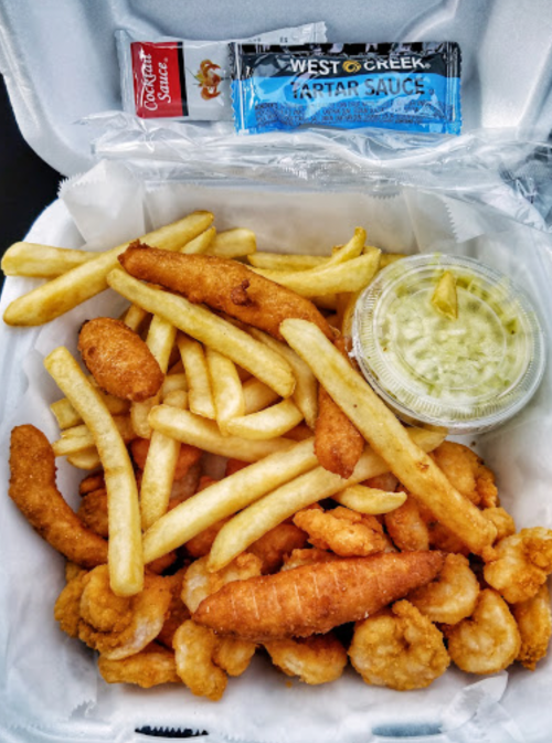 A takeout container filled with fried shrimp, French fries, tartar sauce, and a side of coleslaw.
