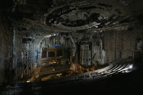 A dark, abandoned theater with intricate, damaged architecture and remnants of a once-grand interior.