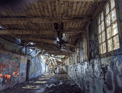 A dilapidated interior of a building with graffiti on the walls and a partially collapsed ceiling.