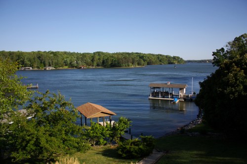 A serene lake view with a dock, gazebo, and lush greenery under a clear blue sky.