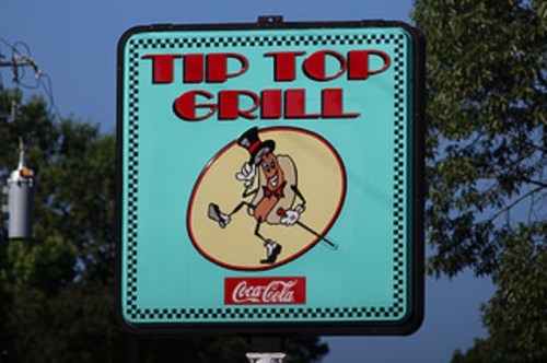 Sign for Tip Top Grill featuring a cartoon hot dog character in a top hat, with a Coca-Cola logo at the bottom.