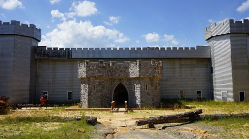 A large, modern castle-like structure with stone and metal features, surrounded by grass and blue skies.