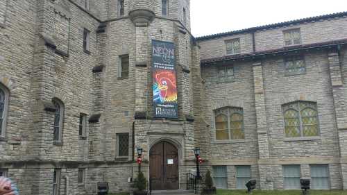 Stone building with a colorful banner advertising an event, featuring large windows and a tower.