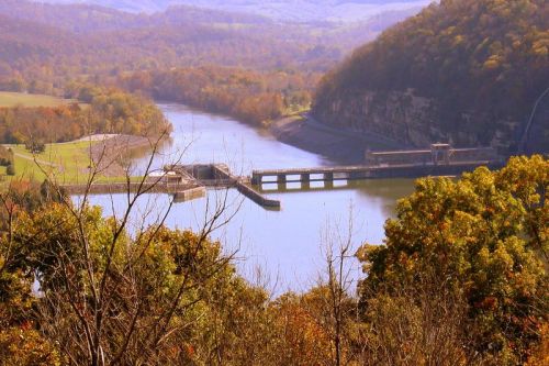 A scenic view of a river and dam surrounded by autumn foliage and rolling hills.