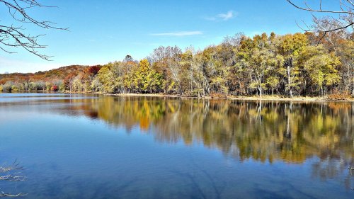 A serene lake reflecting colorful autumn trees under a clear blue sky.