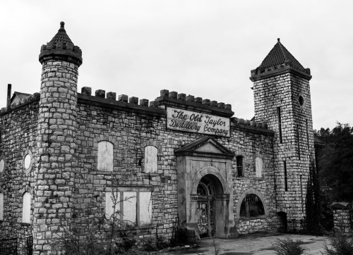 Black and white image of the Old Taylor Distillery, featuring stone walls and castle-like towers, with boarded windows.