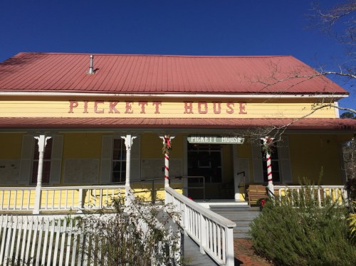A yellow building with a red roof and "Pickett House" sign, featuring a porch and decorative elements.