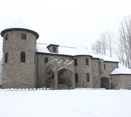 A snow-covered stone castle with turrets and an arched entrance, surrounded by trees in a winter landscape.