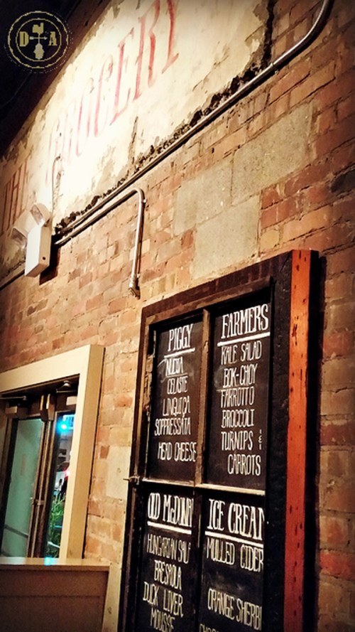 Menu board on a rustic brick wall featuring dishes like piggy salad, farmers' vegetables, and ice cream options.