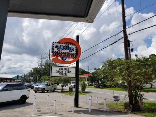 Sign for Willy Burger featuring burgers, onion rings, and shakes, with a cloudy sky in the background.